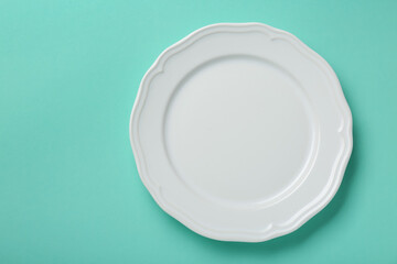 Empty white ceramic plate on turquoise background, top view. Space for text - obrazy, fototapety, plakaty
