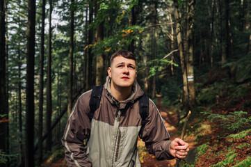 Handsome young man with a stick in his hands is traveling in the mountains, walking on a path in the forest and looking ahead
