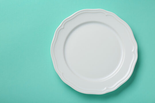 Empty white ceramic plate on turquoise background, top view. Space for text