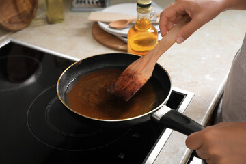 Woman with wooden spatula and frying pan of used cooking oil near stove, closeup