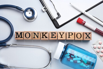 Word Monkeypox made of wooden cubes, pills and stethoscope on light background, flat lay