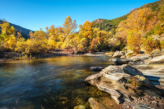 Autumn foliage and dramatic boulders by the Golo river at the Torrent de Cipetto near Barchetta in Corsica