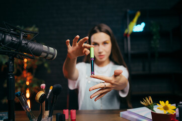 Attractive female blogger shows a tube of cosmetics to the camera and records a beauty video for social networks. The work of a beauty blogger.