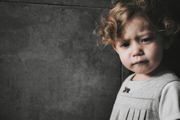 Close-up portrait of a cute little white Caucasian girl with a sad expression on her face, isolated against a dark moody background