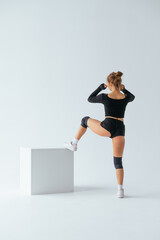 Athletic woman dancer dances twerk on a white cube on a white background. Vertical