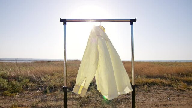 Yellow linen shirt hanging on rail outdoors in the field against sun light, ripple on wind. Cloth made from natural biodegradable fiber. 