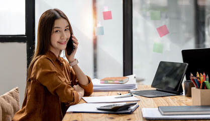 Happy businesswoman talking on mobile phone while analyzing weekly schedule in her notebook.