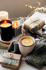 Cozy winter breakfast concept. Tea with lemon, candles, gift box, books and warm knitted sweater on white background. Top view