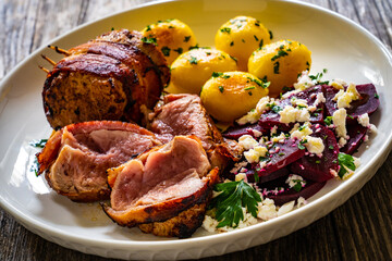 Medium well done pork loin wrapped in bacon with fried potatoes and feta cheese on beets on wooden table
