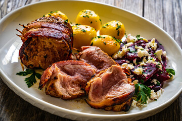 Medium well done pork loin wrapped in bacon with fried potatoes and feta cheese on beets on wooden...