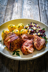 Medium well done pork loin wrapped in bacon with fried potatoes and feta cheese on beets on wooden table

