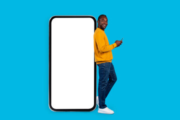 Stylish cool black man posing by huge smartphone on blue