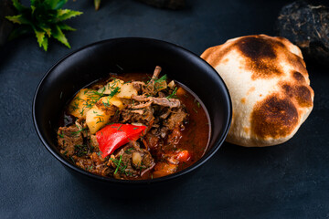 Stewed beef with potatoes, sweet peppers, onions in tomato sauce with herbs and flatbread in a bowl.
