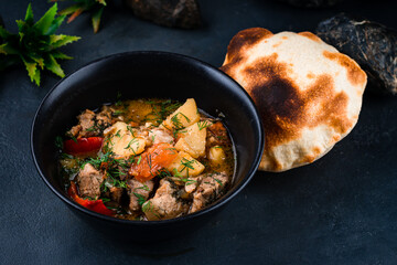 Fresh stewed pork with potatoes, sweet peppers, tomatoes, onions in tomato sauce with herbs and flatbread in a bowl.
