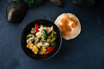 Chicken stew with cauliflower, corn, zucchini, bell peppers, onions, herbs in a bowl and tortilla.