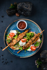 Kebab, barbecued chicken on a stick with tomatoes, lettuce, onion, arugula, sour cream, tortilla and red sauce.