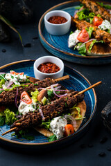 Set of kebab, barbecued beef and chicken on a stick with tomatoes, lettuce, onion, arugula, sour cream, tortilla and red sauce in a plates.