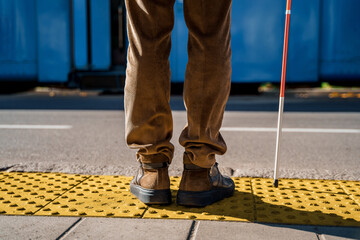 Blind man with a cane stopped on a tactile tile in front of a tram obstacle