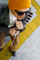 Blind man with a walking stick sitting on a bench in the city