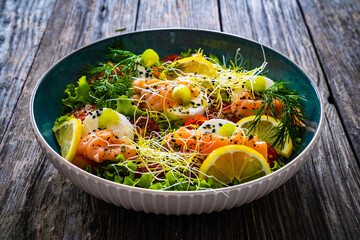 Salmon salad - smoked salmon, goat cheese and fresh vegetables on wooden table
