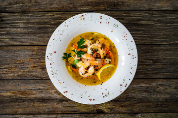 Roast prawns in butter sauce with lemon, garlic and parsley on wooden table
