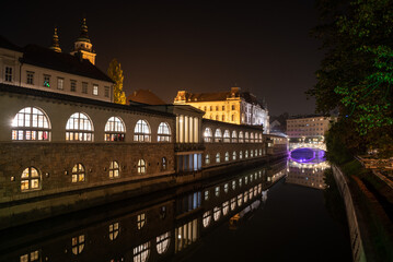 Iconic building of the central market in Ljubljana illuminated at night, the bridge of Preseren sqare in the background