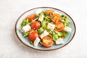 Vegetarian salad of tomatoes, marigold, microgreen, feta cheese on gray. Side view.