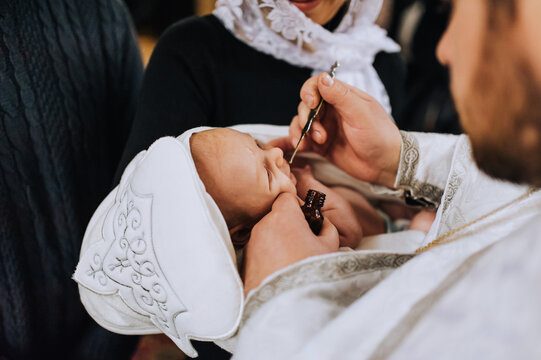 The priest in the church conducts a sacred rite, the ritual of anointing the head of a newborn child. Close-up photography, religion.