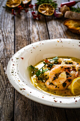 Roast prawns in butter sauce with lemon, garlic and parsley on wooden table
