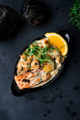 Baked red fish salmon with mushrooms, potatoes, cheese and sauce, garnished with herbs and lemon.