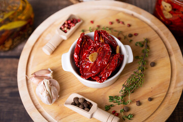 Sun-dried tomatoes in olive oil in a white bowl with pepper, garlic and thyme on a wooden board. Home cooking, rustic style. Selective focus, close-up.