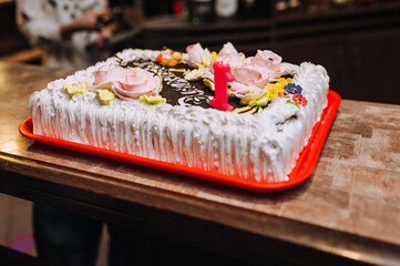A beautiful large rectangular cake decorated with flowers, candles with the number one. Children's birthday, baking.