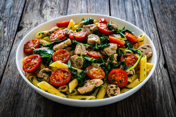 Roasted chicken nuggets, cherry tomatoes, spinach and penne served on wooden table
