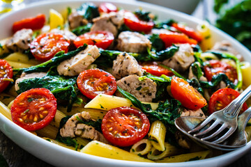 Roasted chicken nuggets, cherry tomatoes, spinach and penne served on wooden table
