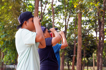 Three Asian boys use binoculars to look at birds in a community forest. own. The concept of learning from learning sources outside the school. Focus on the first child.