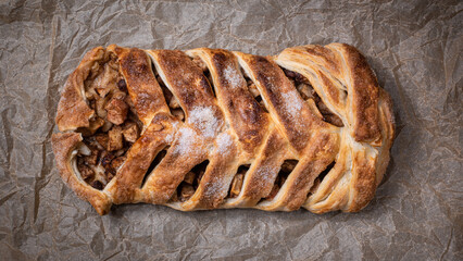 Delicious homemade sweet pigtail pie with apples on baking parchment top view.