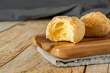 bitten pão de queijo, a traditional brazilian food made of chesse bread, over wooden table and cutting board