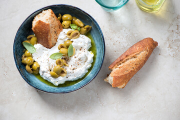 Bowl with ricotta, crusty bread, green olives and olive oil on a light-beige stone background, horizontal shot, flat lay