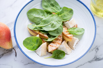 Plate with fresh spinach, grilled pear and camembert salad, horizontal shot on a white marble background, middle close-up