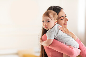 Young mom holding and hugging adorable baby, enjoying motherhood and child care, standing in bedroom at home