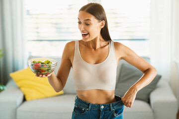 Successful weight loss diet. Excited slim lady holding bowl with vegetable salad and showing result...
