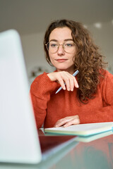Young woman student using laptop elearning, remote working at home office looking at computer...