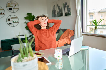Young pretty woman taking rest break relaxing while remote working from home sitting on chair at...