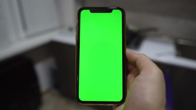 Use green screen for copy space closeup. indoors of toilet or bathroom. Chroma key mock-up on smartphone in hand. young man holds mobile phone iPhone and swipes photos or pictures