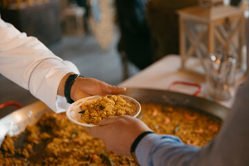 close up view of a waiter's hand delivering a plate of paella