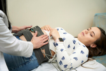 Woman pregnant checking fetal heart beat by fetal monitoring. Female doctor gynecologist putting...