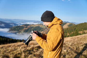 Fototapeta premium Photographer working outdoor. Taking photos in mountains. Nature photographer in action. Silhouette of a landscape photographer in twilight.