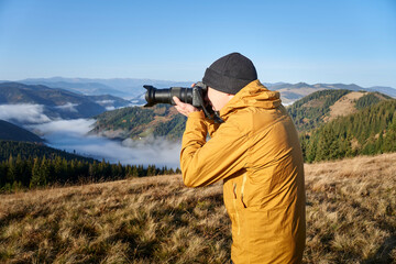 Photographer working outdoor. Taking photos in mountains. Nature photographer in action. Silhouette of a landscape photographer in twilight.
