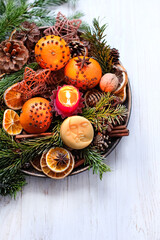 Christmas holiday. Winter altar for Yule sabbat. Moon amulet, candle, cinnamon, nuts, cones, decorated oranges and dry orange slices, fir branches in plate on wooden table. Festive winter season