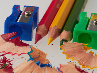 some colored pencils of different colors and a pencil sharpener and pencil shavings on a white background